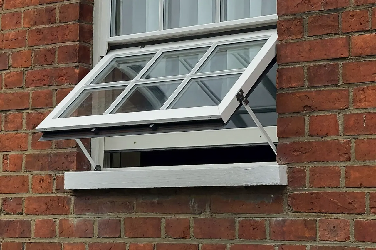 A top-hung casement window shown part-open on a brick house